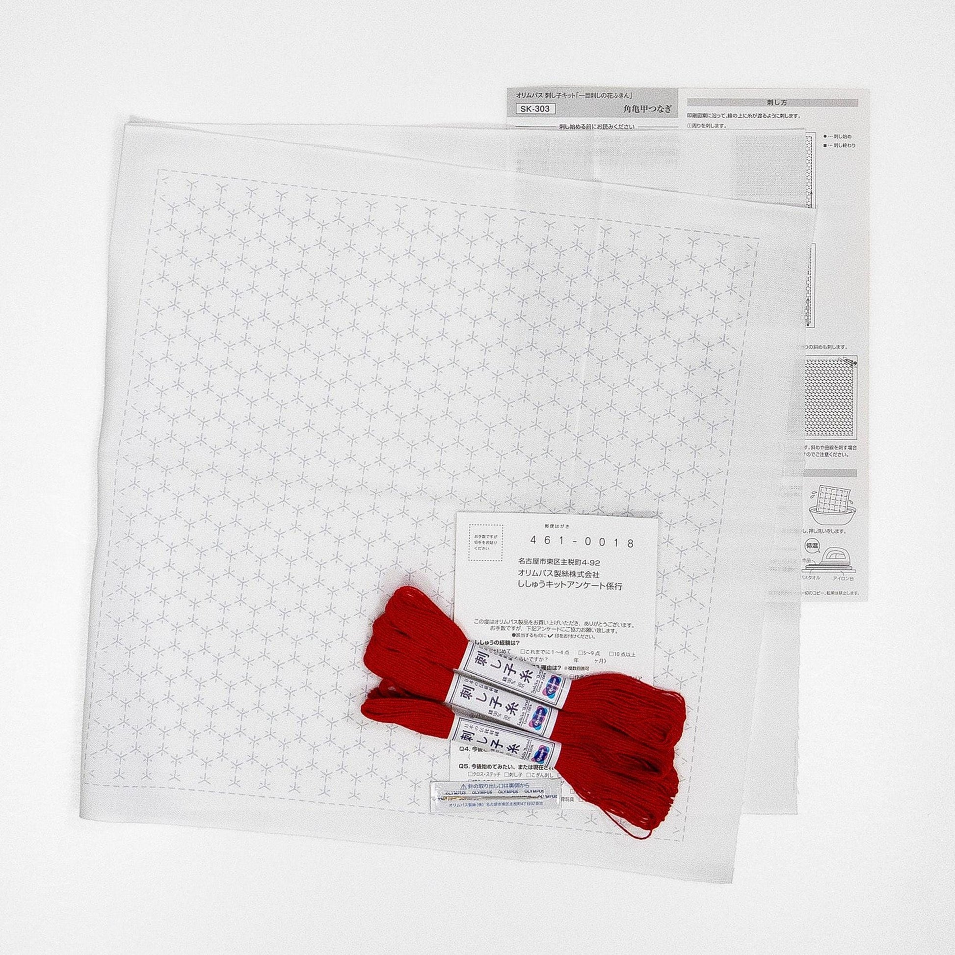 a white fabric with a geometric pattern, along with a pair of red embroidery floss and a piece of paper with instructions or information related to the fabric and embroidery.
