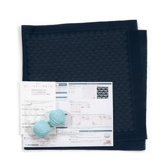 a black fabric with a geometric pattern, a white paper with Japanese text, and two blue balls of yarn.