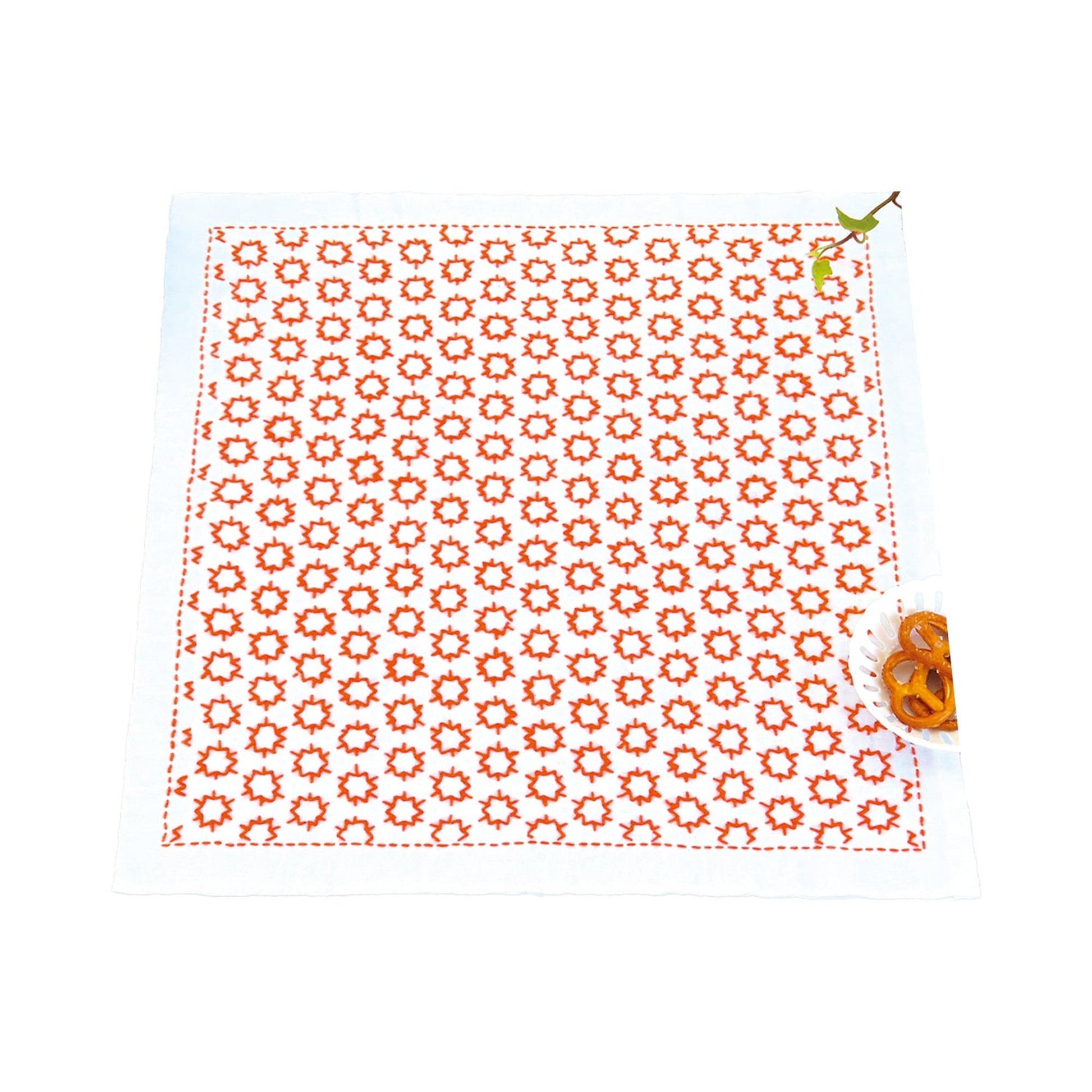 a square napkin with a red and white polka dot pattern, placed on a white surface. Next to the napkin, there is a small bowl containing orange pretzels.