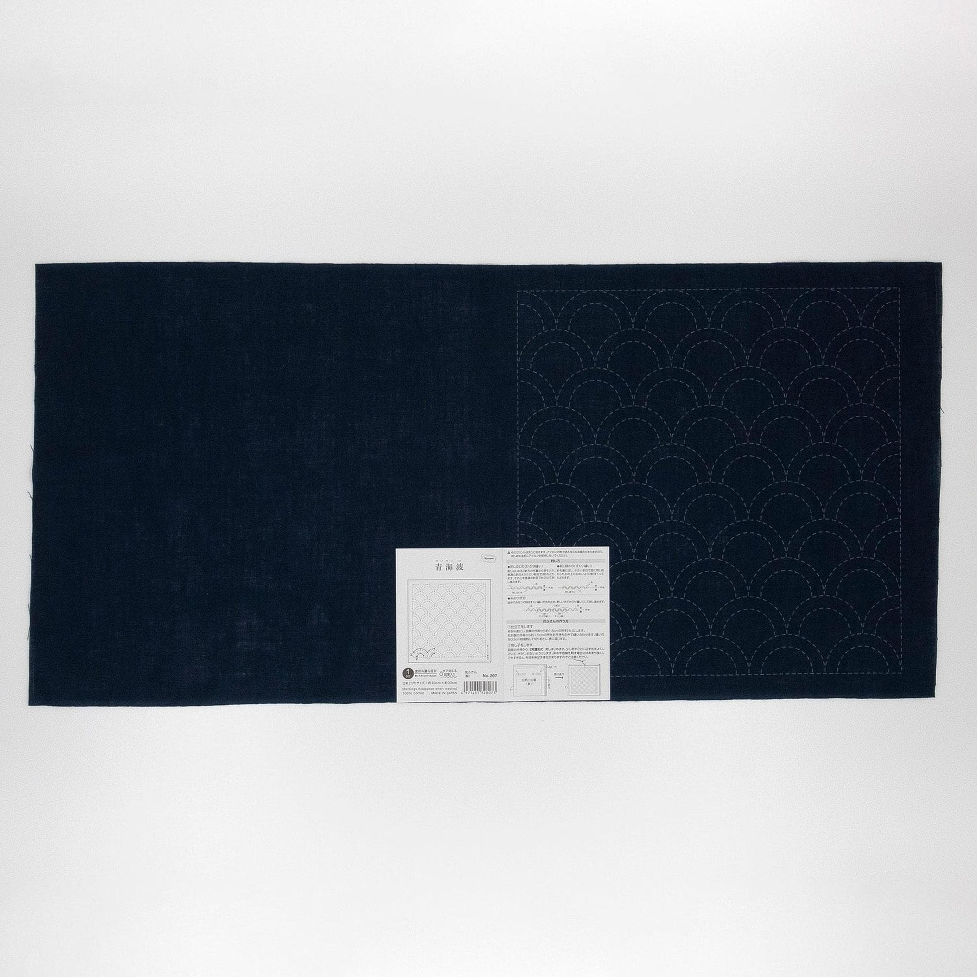 a dark blue fabric with a white pattern on it, placed on a white background. There is a small white label or instruction sheet attached to the fabric, but the text is not legible.