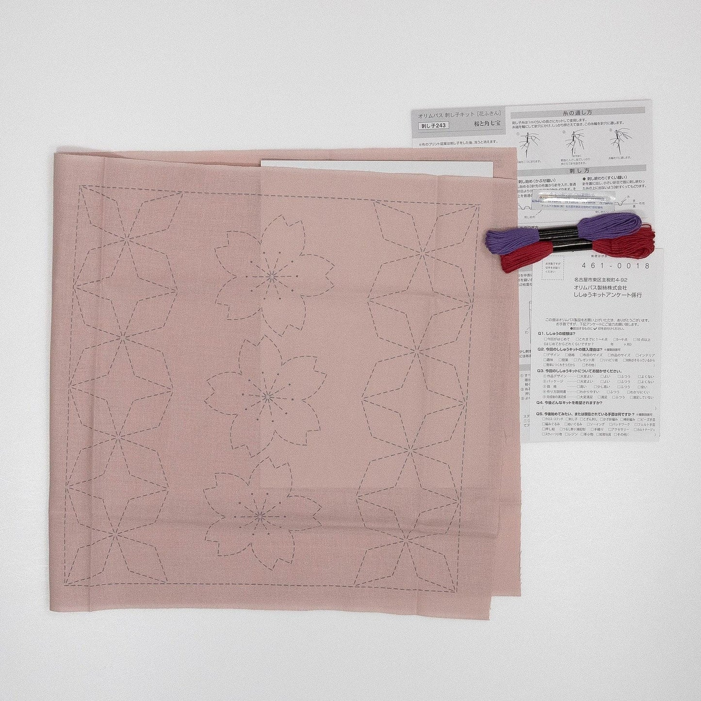 a pink fabric with a pattern of flower-like designs, along with a piece of paper and some thread, suggesting a sewing or crafting project.