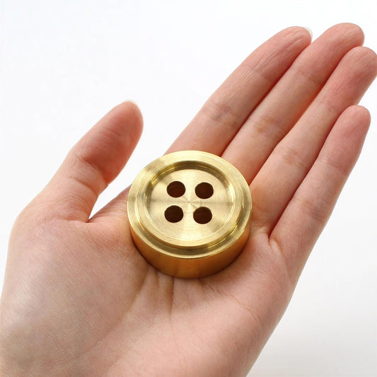 A hand holding a golden button with four holes.
