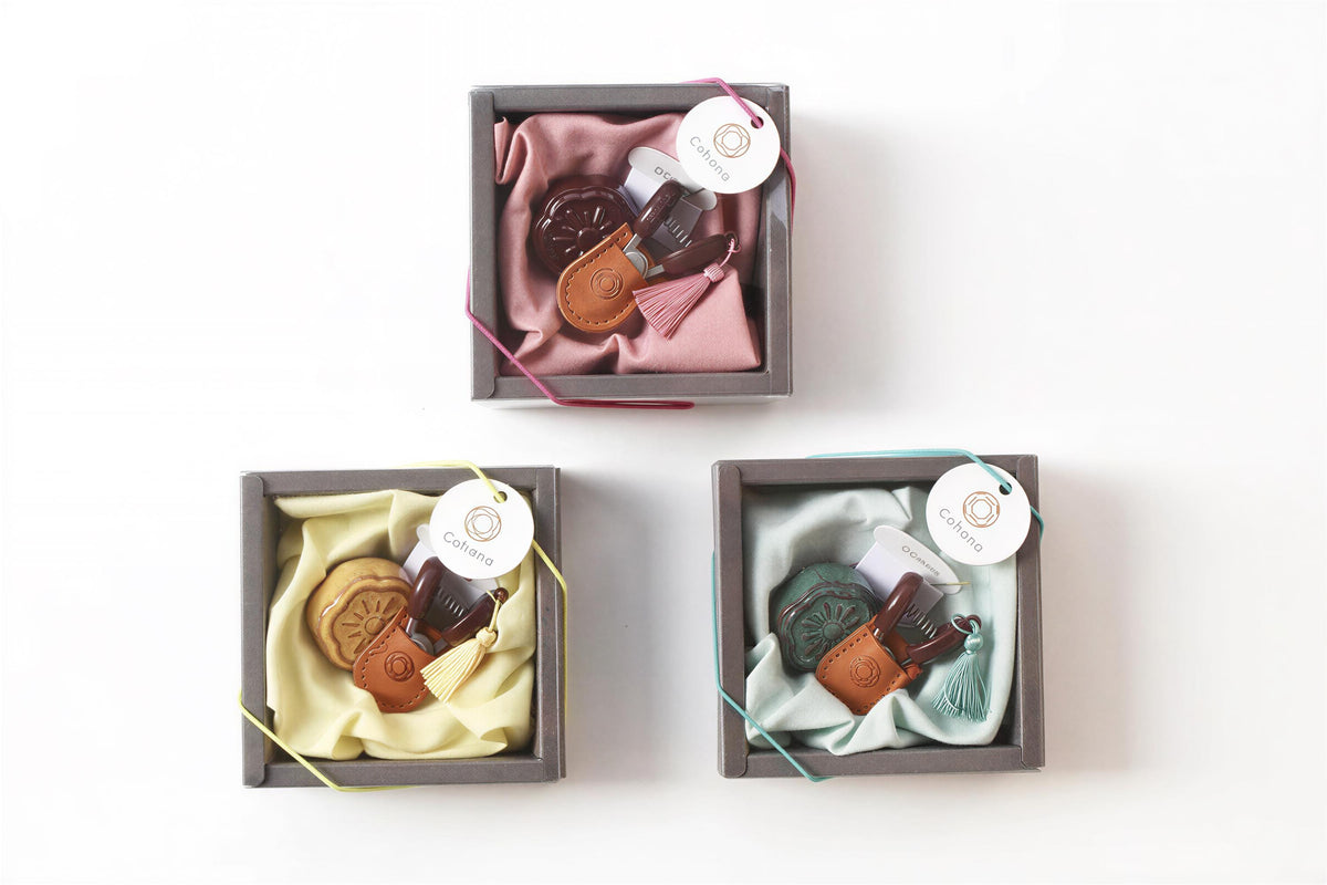 three small gift boxes with various items inside, including a pink velvet cloth, a brown leather item, and a green cloth.