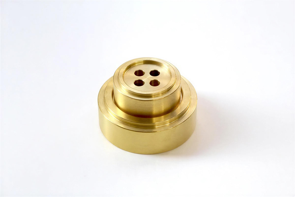 A brass-colored metal object with a circular hole in the center, sitting on a white background.