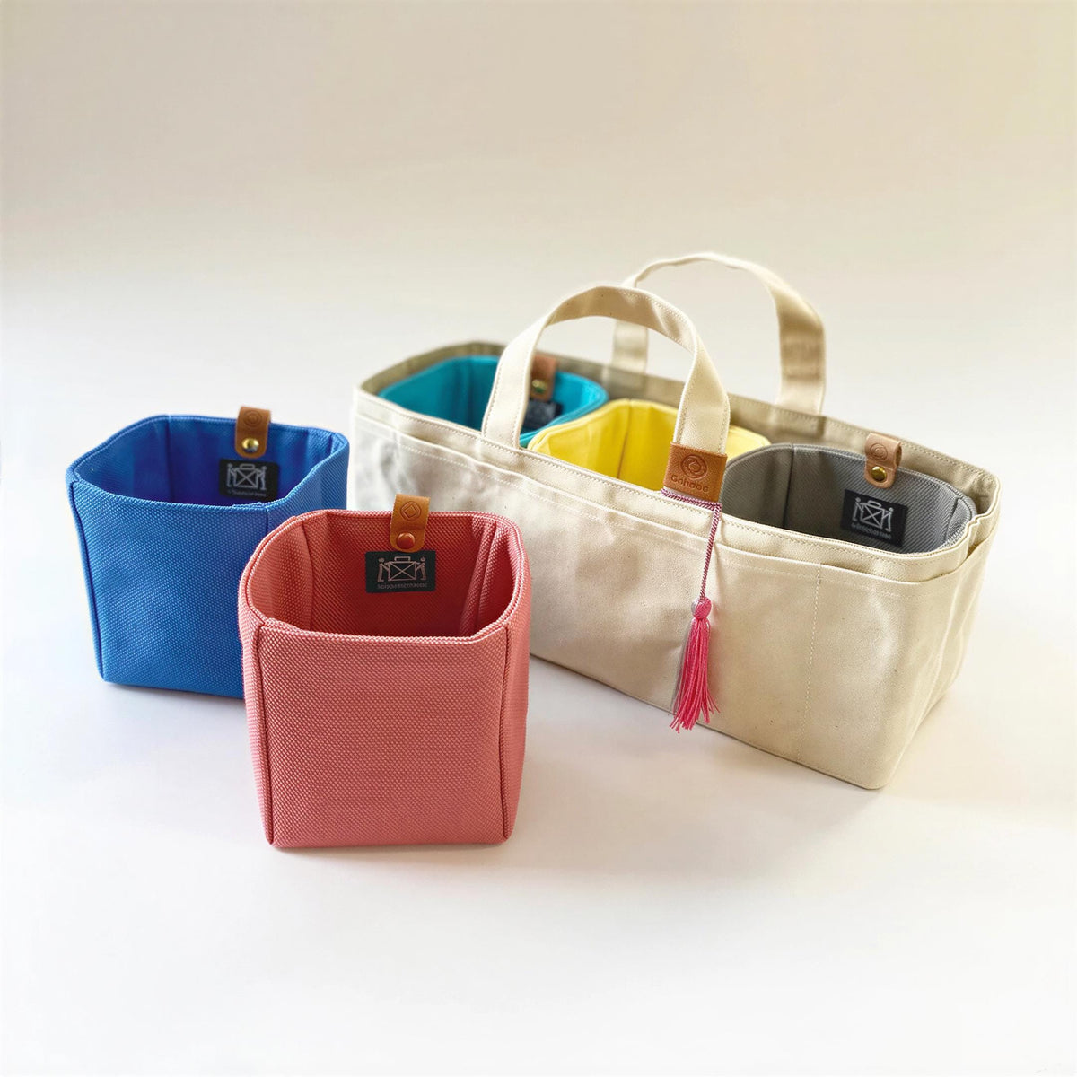 a collection of colorful fabric containers, including a blue container, a pink container, and a beige container, arranged on a white background.