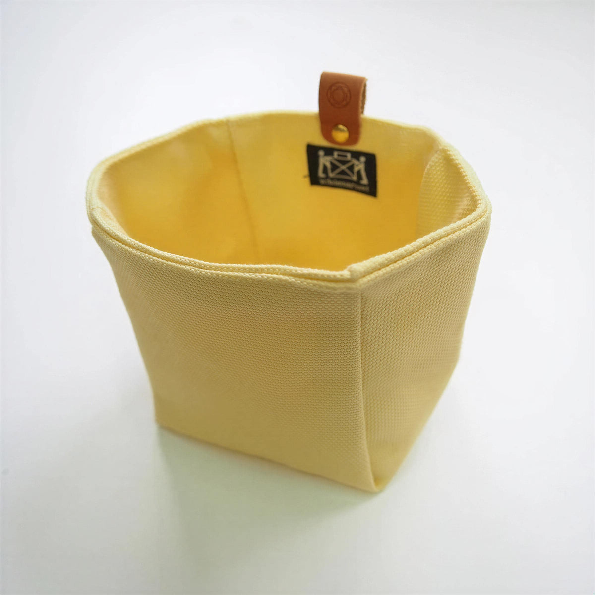 A yellow, textured fabric container with a leather tag attached to it.