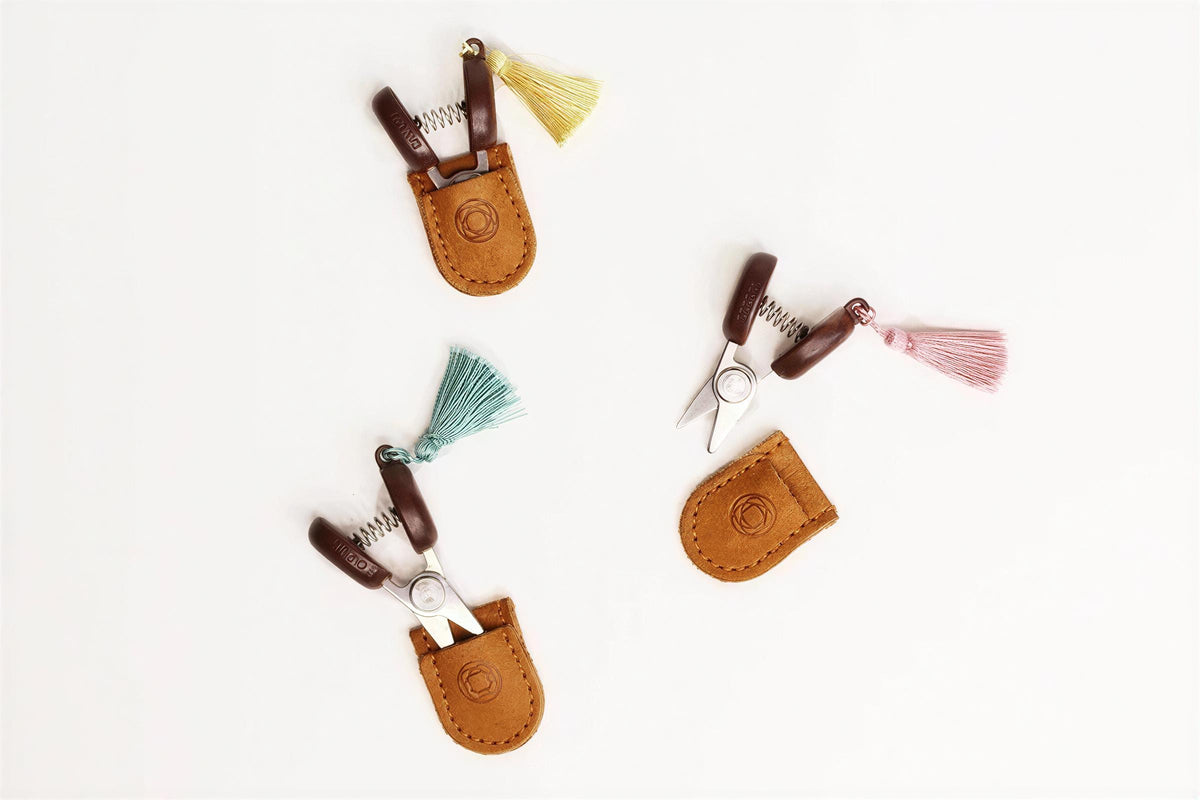 three pairs of scissors with tassels, each pair placed in a brown leather pouch.
