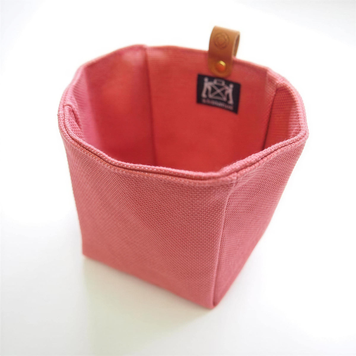 A pink woven basket with a leather tag attached to it.