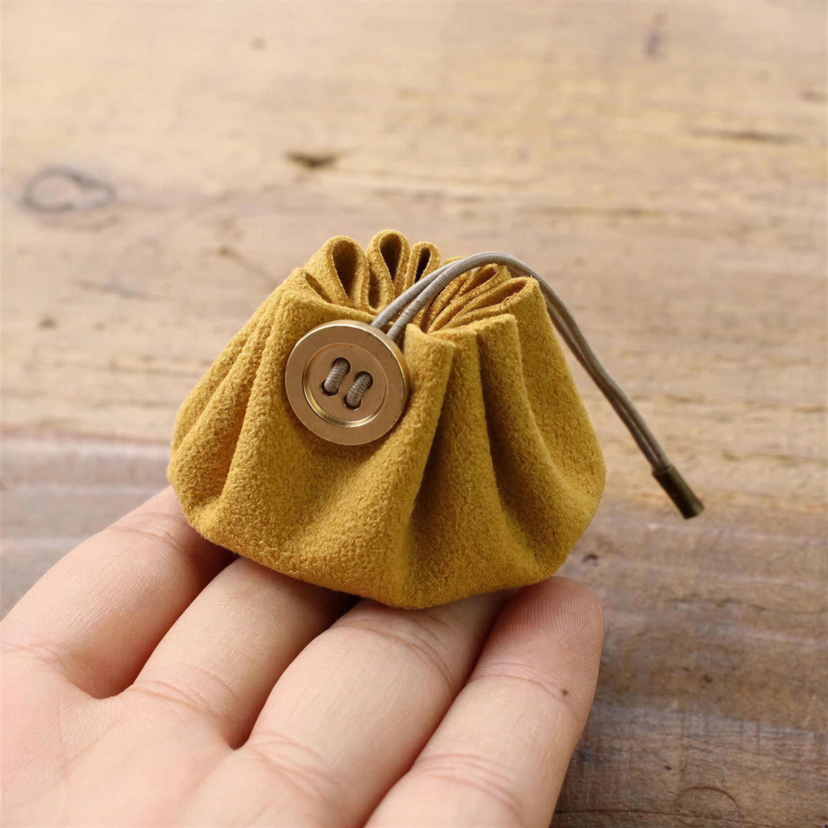 A hand is holding a small, yellow pouch with a button closure.