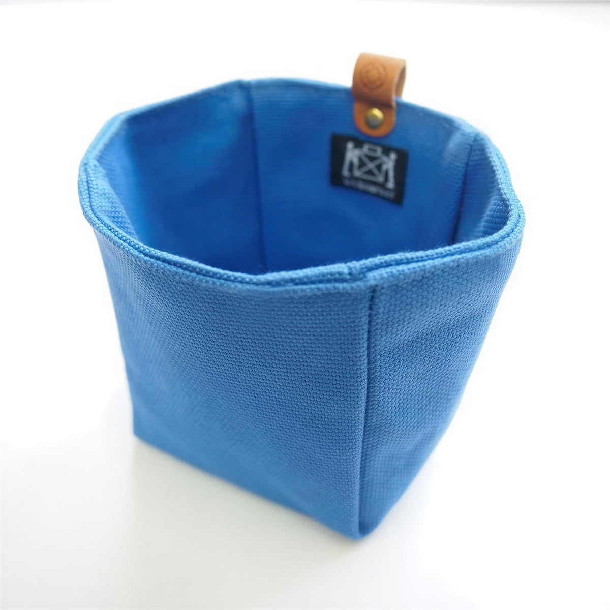 A blue, textured fabric container with a leather tag attached to it.