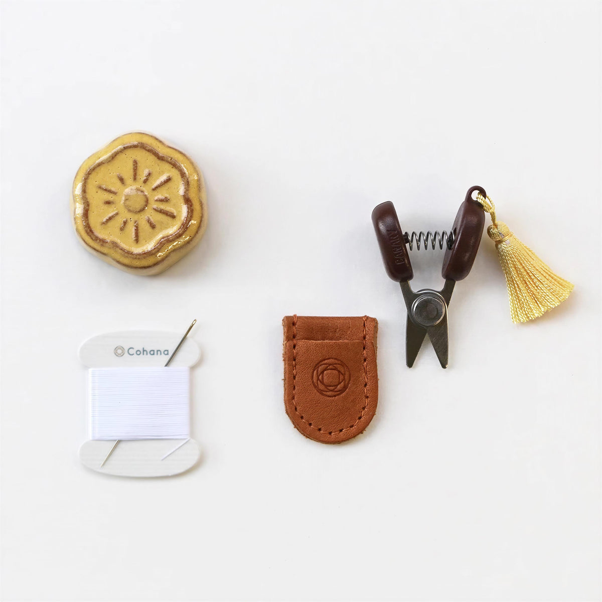 various sewing and crafting tools, including a pair of scissors, a spool of thread, a small leather pouch, and a round object resembling a flower or button.