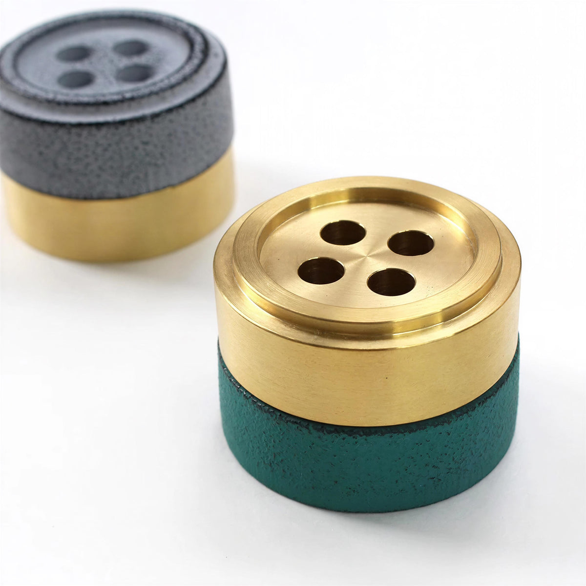 two metal objects with a combination of green and gold colors. One object is a metallic container with a green base and a gold top, while the other is a metallic button with a gray top and a gold base.