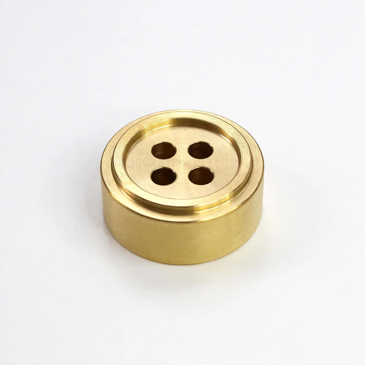 A brass button-like object with four holes, sitting on a white background.