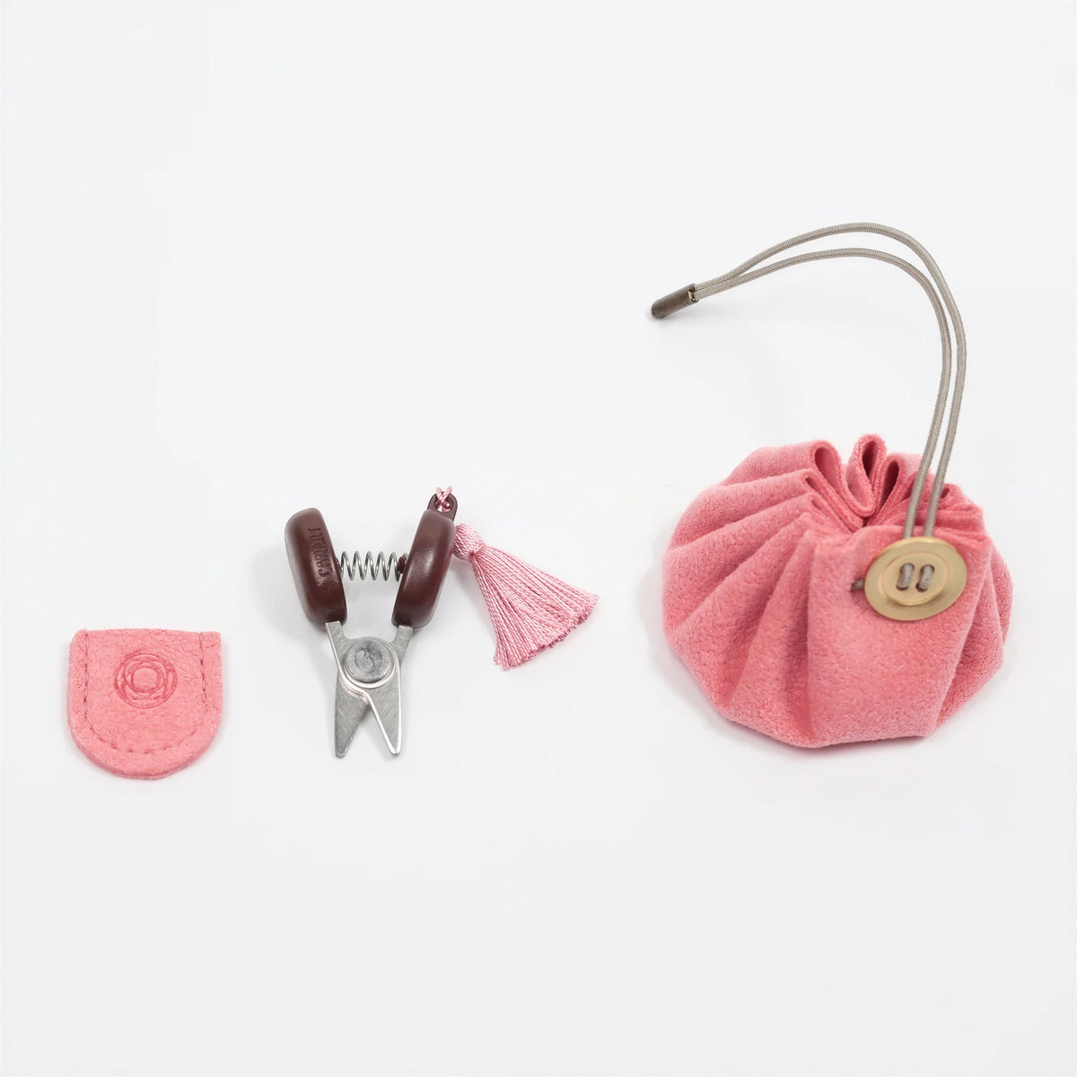 a pink pouch with a tassel, a pair of scissors, and a small pink object, all arranged on a white background.