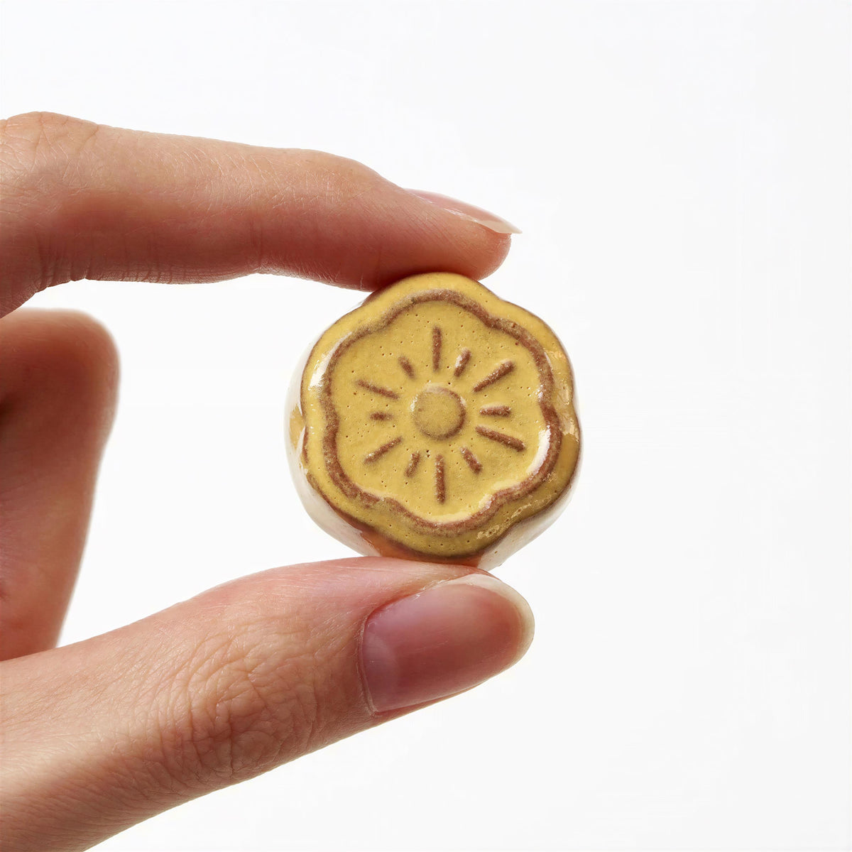 A hand is holding a small, yellow flower-shaped object with a sun-like design on it.