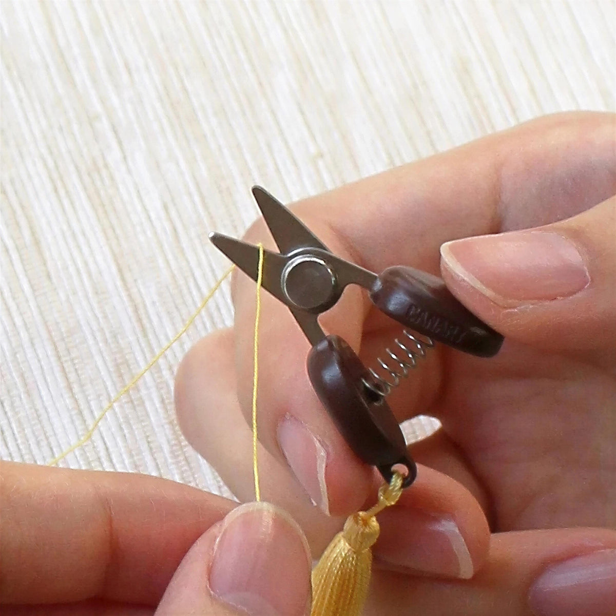 A pair of hands holding a small pair of scissors with a tassel attached to the blades.