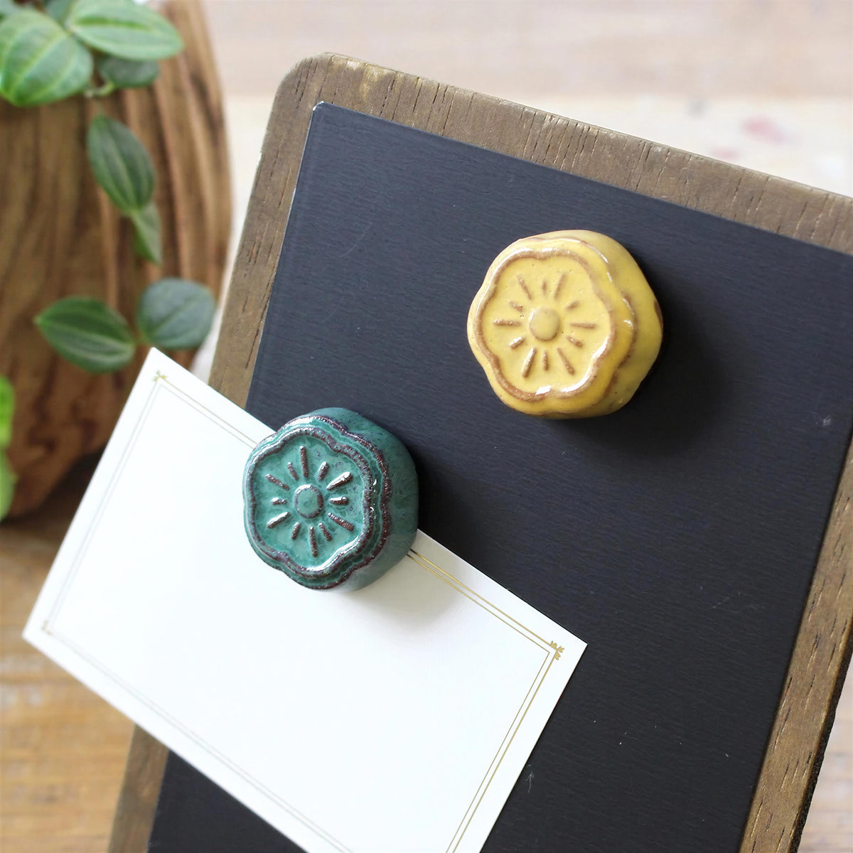 two ceramic magnets with flower-shaped designs, attached to a blackboard or chalkboard.