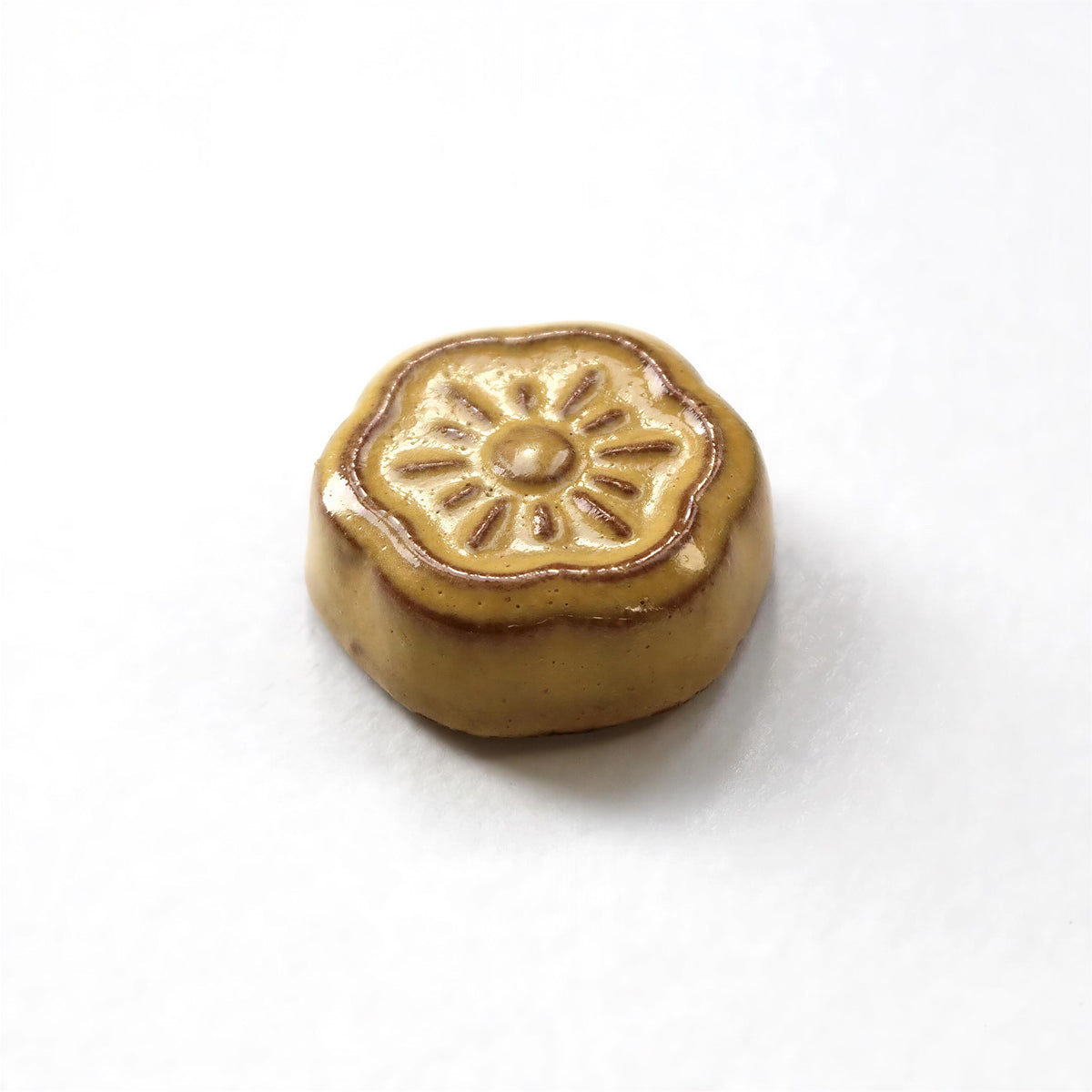 A single, round, brown object with a sun-like design on top, sitting on a white surface.