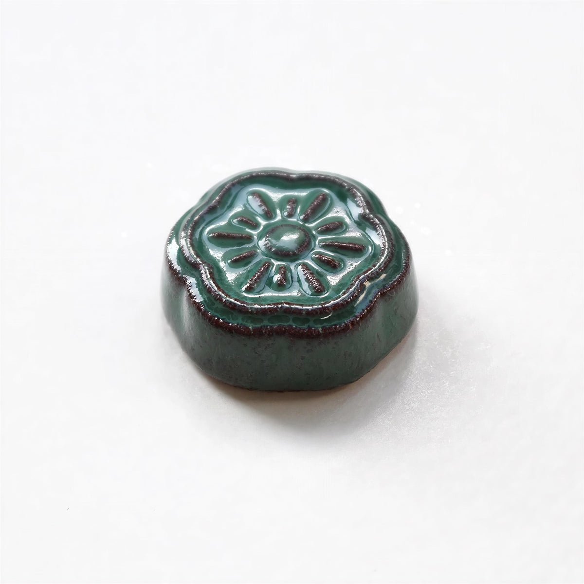 A small, green ceramic object with a flower-like design on it, sitting on a white surface.