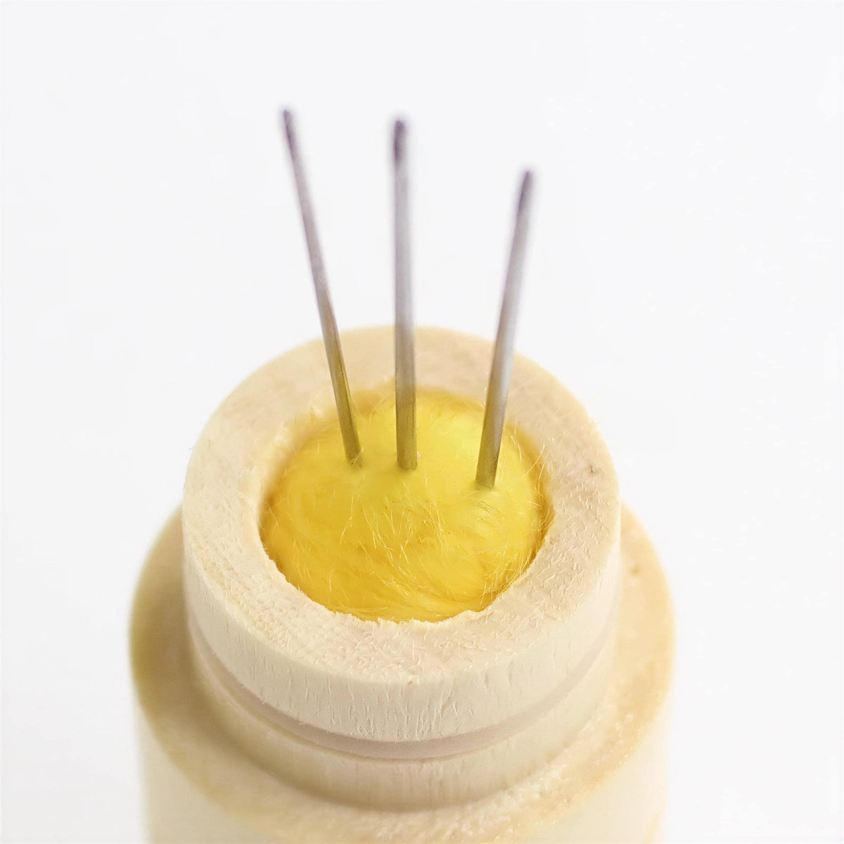 A close-up view of a wooden container with three needles protruding from it, against a white background.