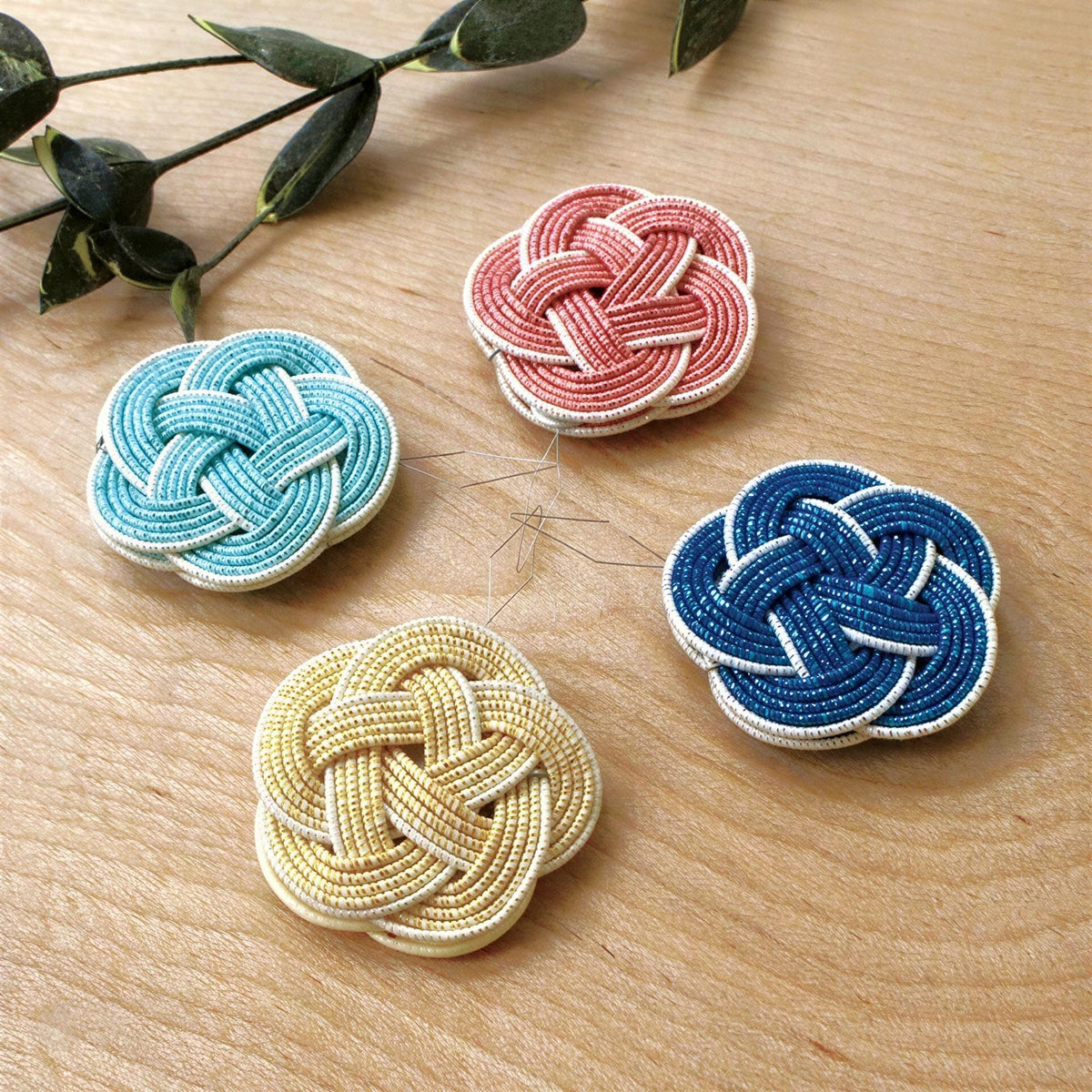 four colorful beaded pieces arranged on a wooden surface, with a green plant leaf visible in the background.
