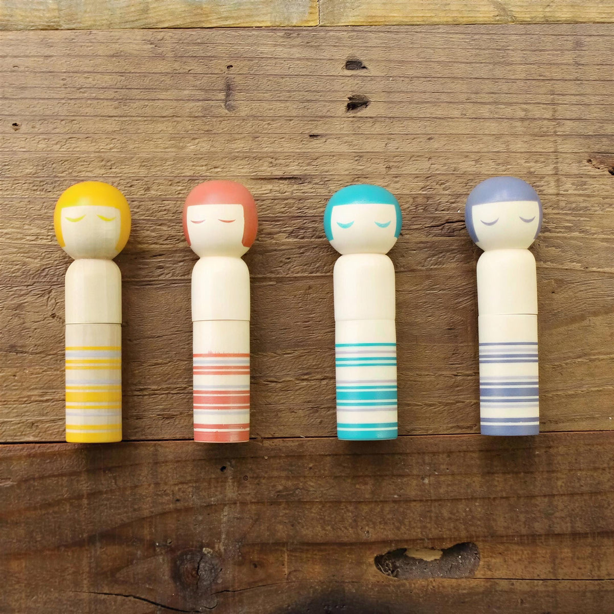Four colorful wooden dolls with closed eyes are arranged on a wooden surface.