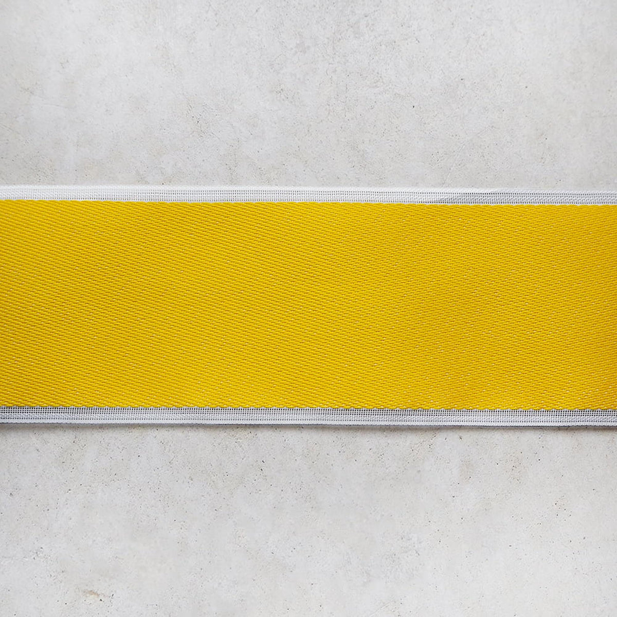 A close-up view of a yellow fabric or ribbon with a white border, placed against a plain white background.