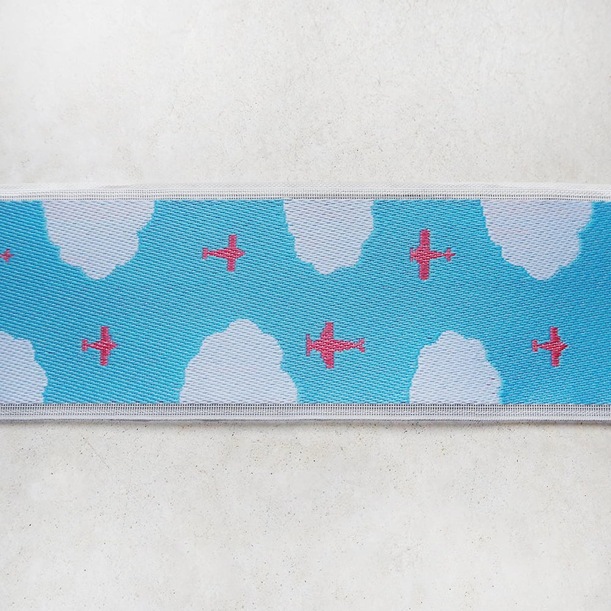 A close-up view of a fabric with a pattern of red airplanes flying through a blue sky with white clouds.