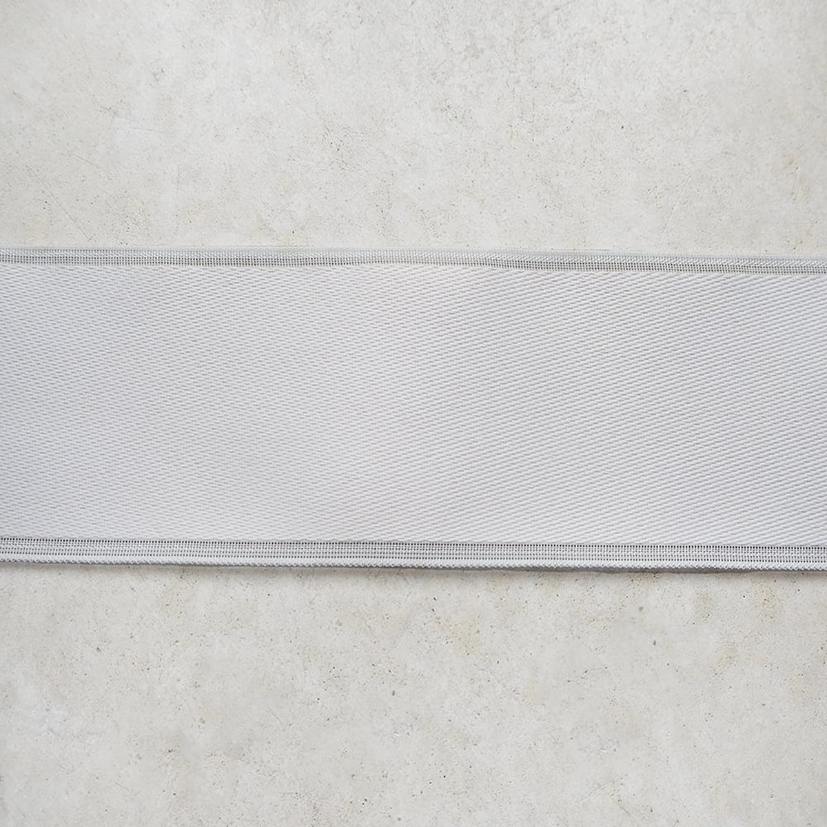 A close-up view of a white fabric or material, possibly a ribbon or ribbon-like material, placed on a textured surface.
