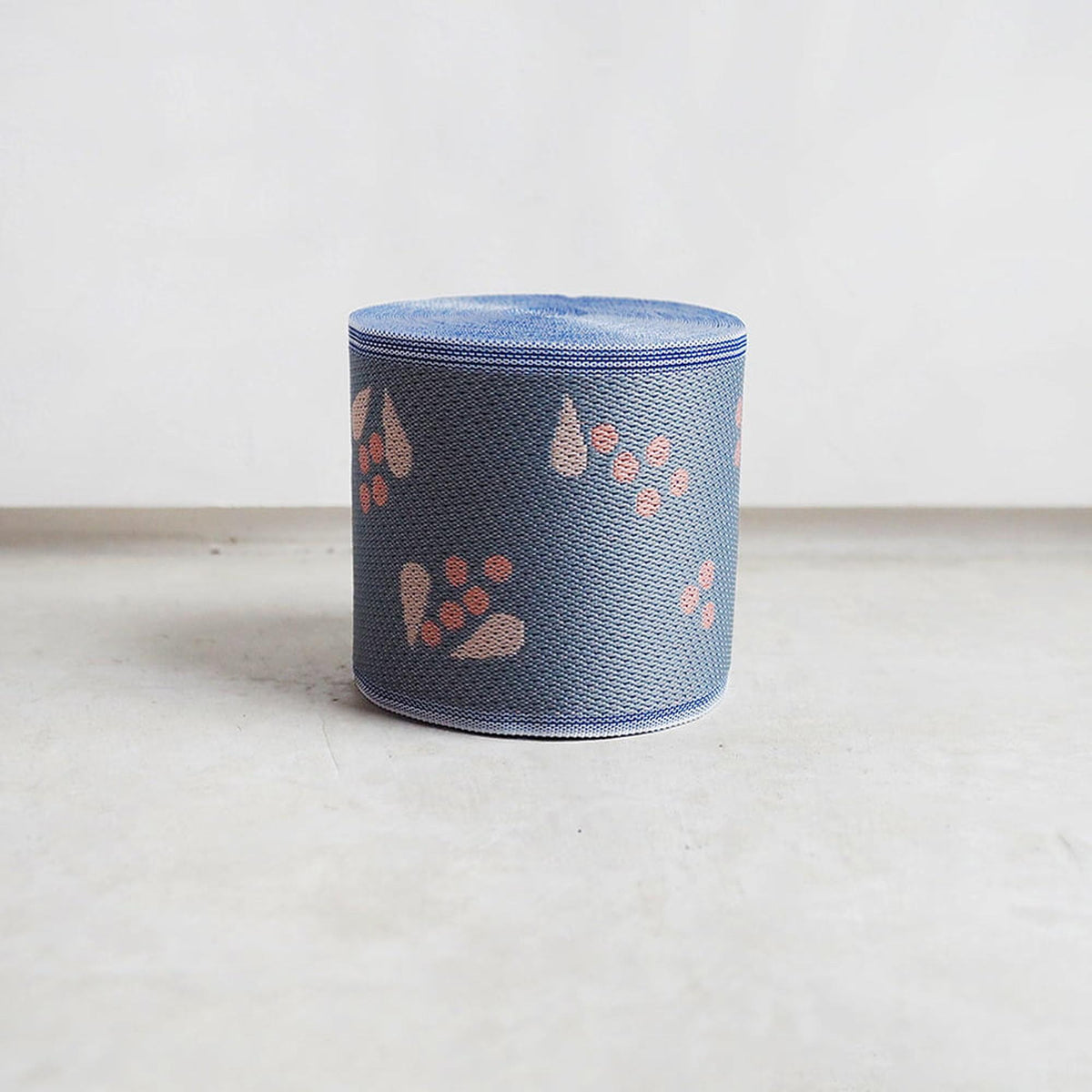 A blue cylindrical object with a pattern of orange and pink flowers on it, sitting on a white surface.
