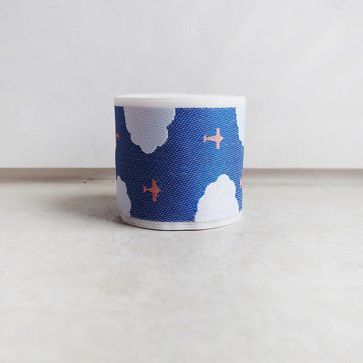 A white object with a blue cloud pattern and two small orange airplanes printed on it, sitting on a white surface.