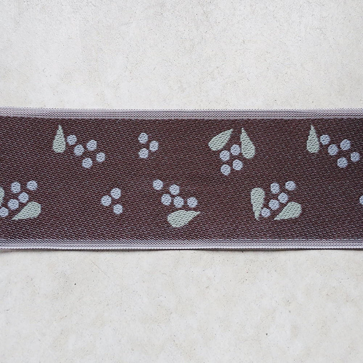 a close-up view of a brown fabric with a repeating pattern of white circles and green leaves.