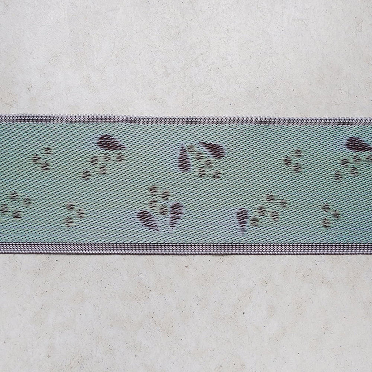 a close-up view of a fabric with a repeating pattern of paw prints in shades of green and purple.