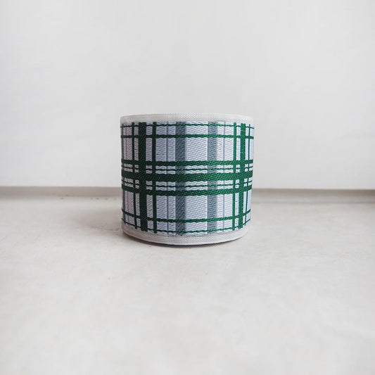 A white and green plaid-patterned object, possibly a container or lampshade, is placed on a white surface against a plain background.