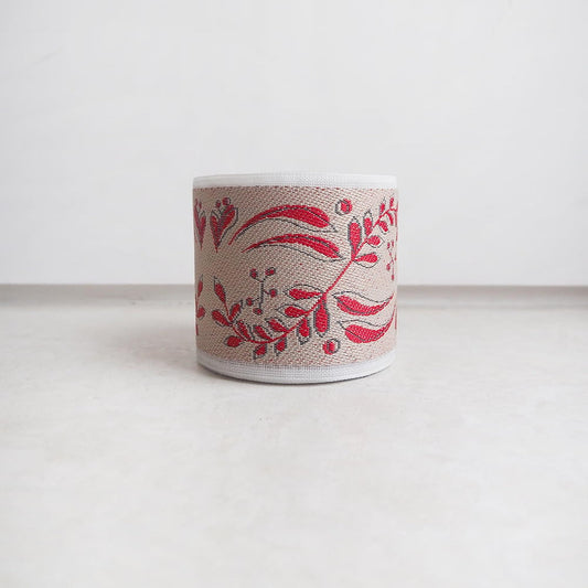 A beige-colored lampshade with a red floral pattern on it, placed on a white surface.