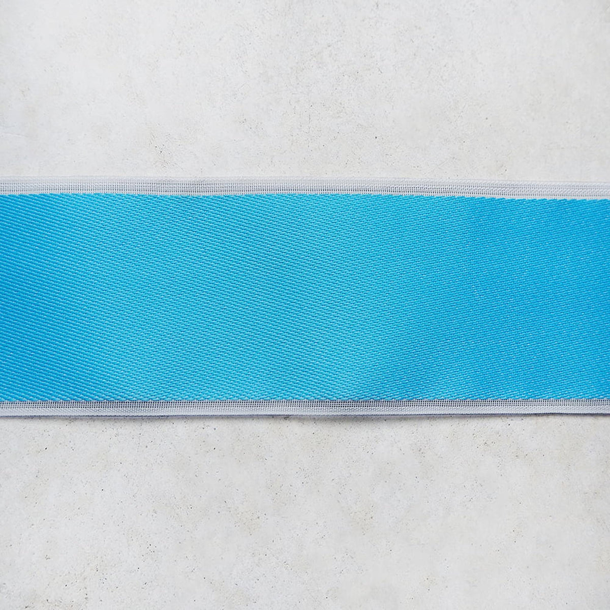 A close-up view of a blue ribbon or fabric with a white border, placed on a white surface.