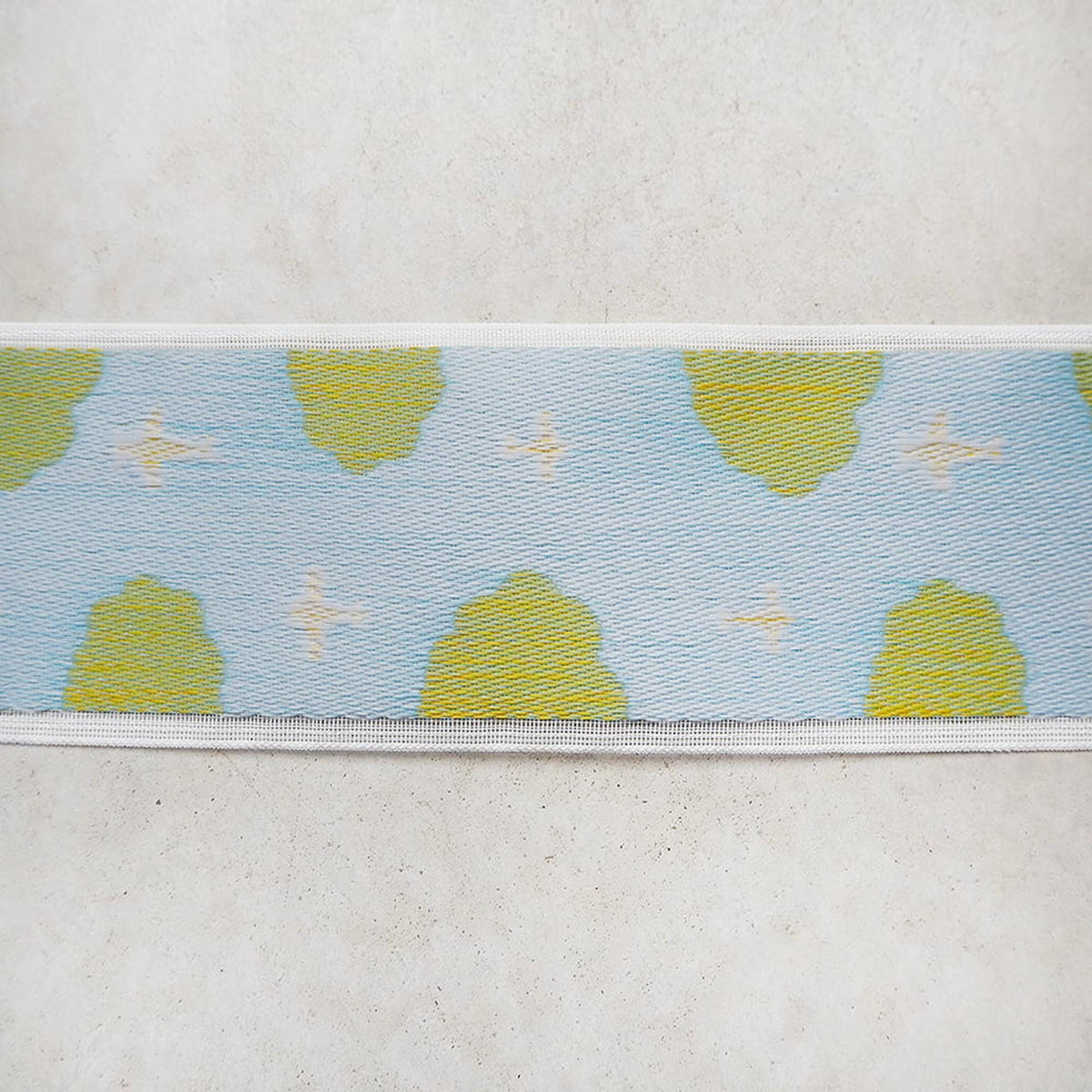 a close-up view of a fabric with a repeating pattern of yellow and blue shapes, resembling clouds or leaves.