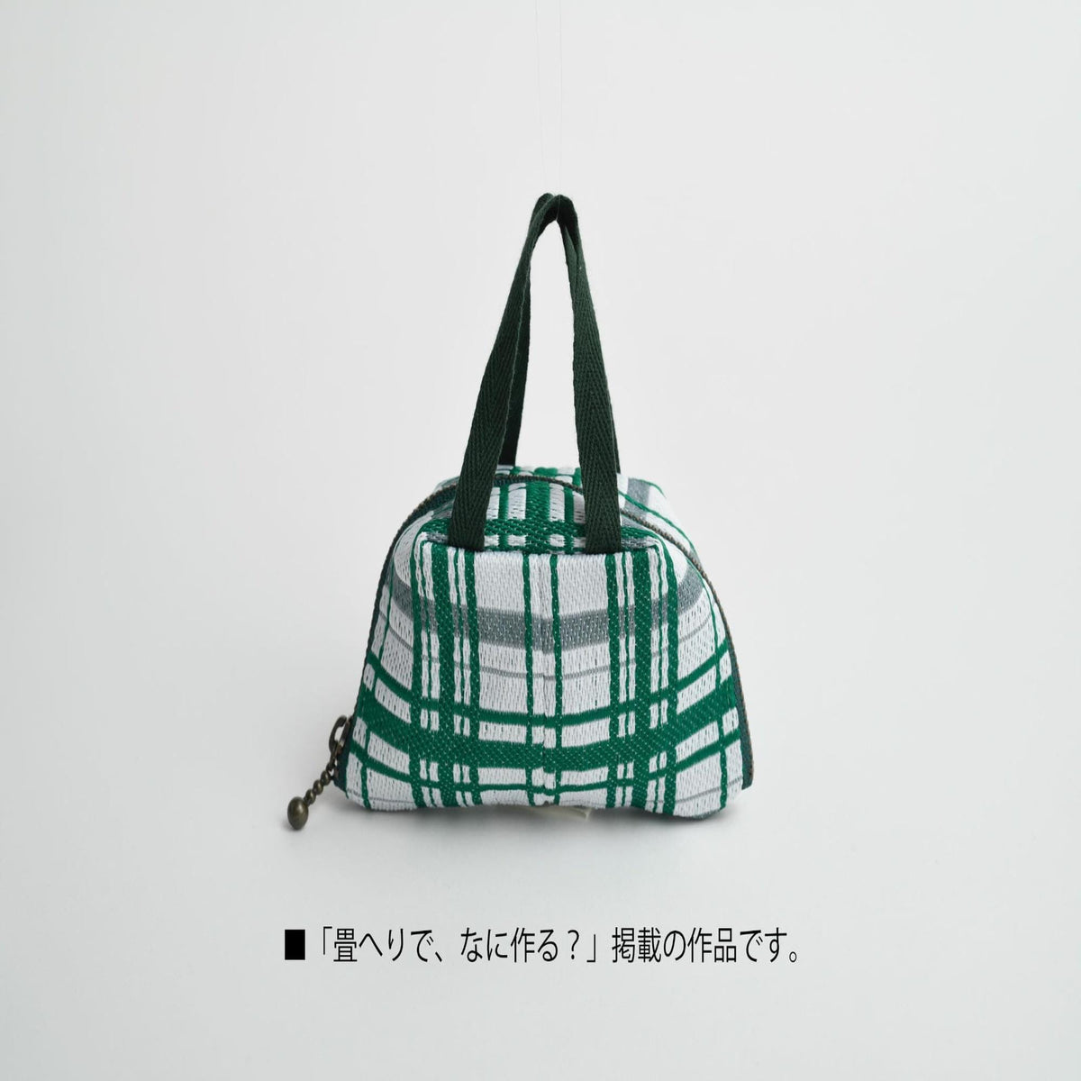 A small green and white checkered bag with a black handle, sitting on a white background.