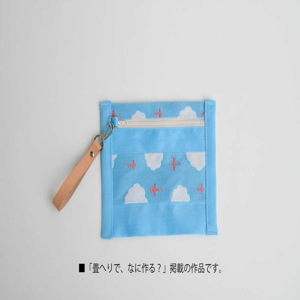 A blue fabric pouch with a cloud and airplane pattern, attached to a leather strap.