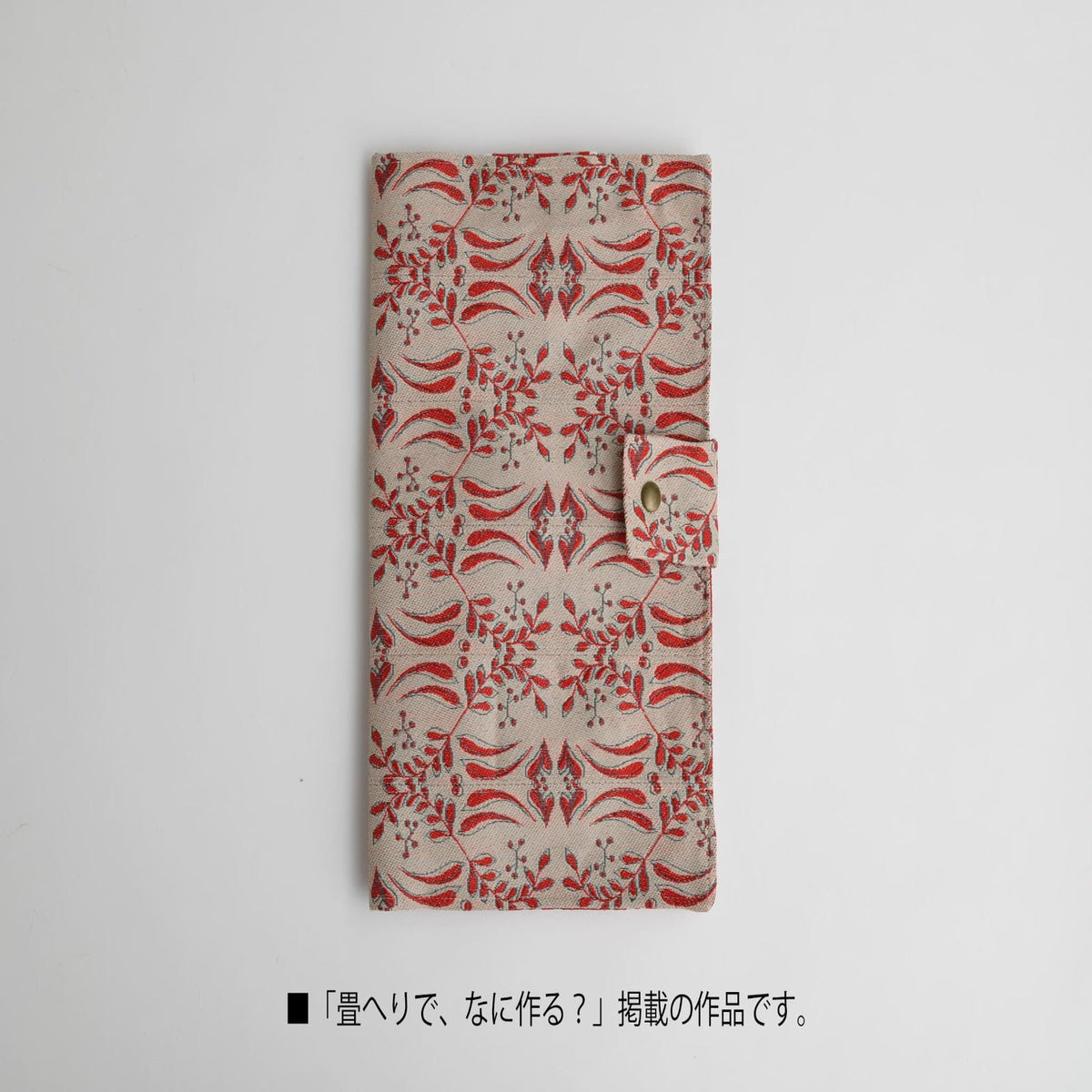 A beige wallet with a red floral pattern printed on it, placed against a white background.