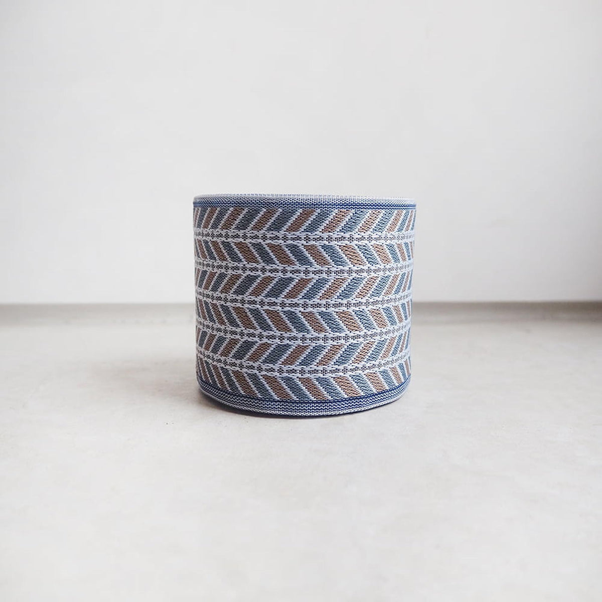 A round, woven object with a geometric pattern in shades of blue and brown, sitting on a white surface.