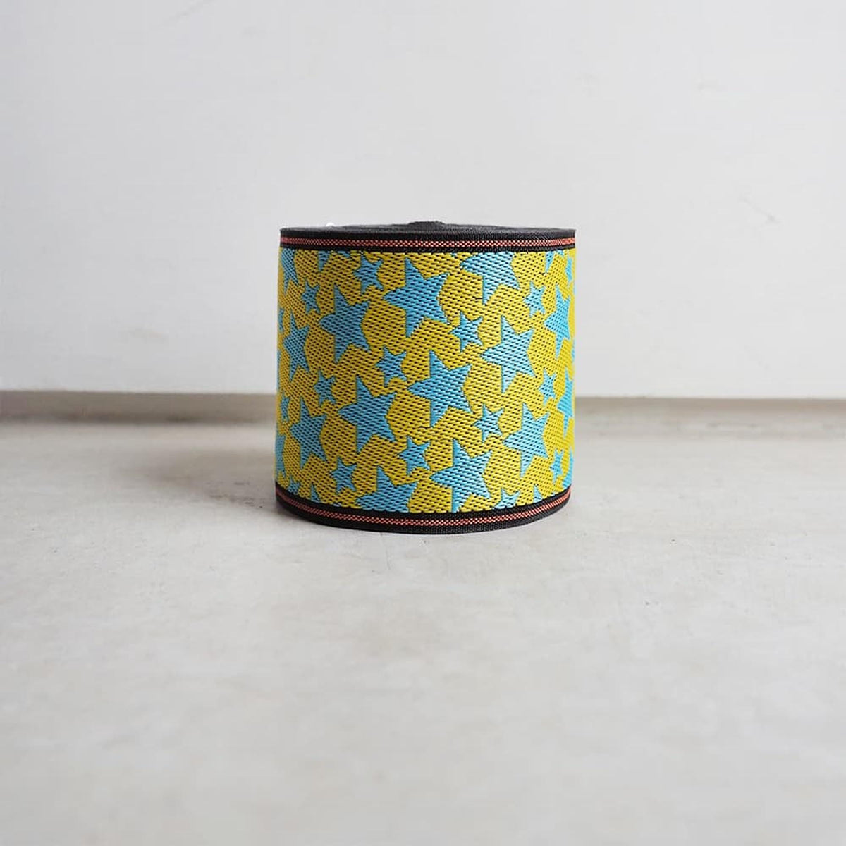 A colorful woven bracelet with a pattern of yellow and blue leaves or flowers is displayed against a plain white background.