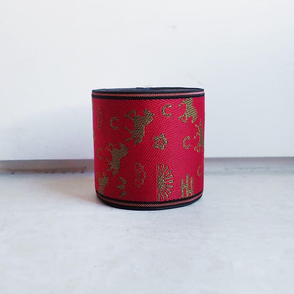 A red and gold decorative band with a pattern of gold shapes and text on a white background.