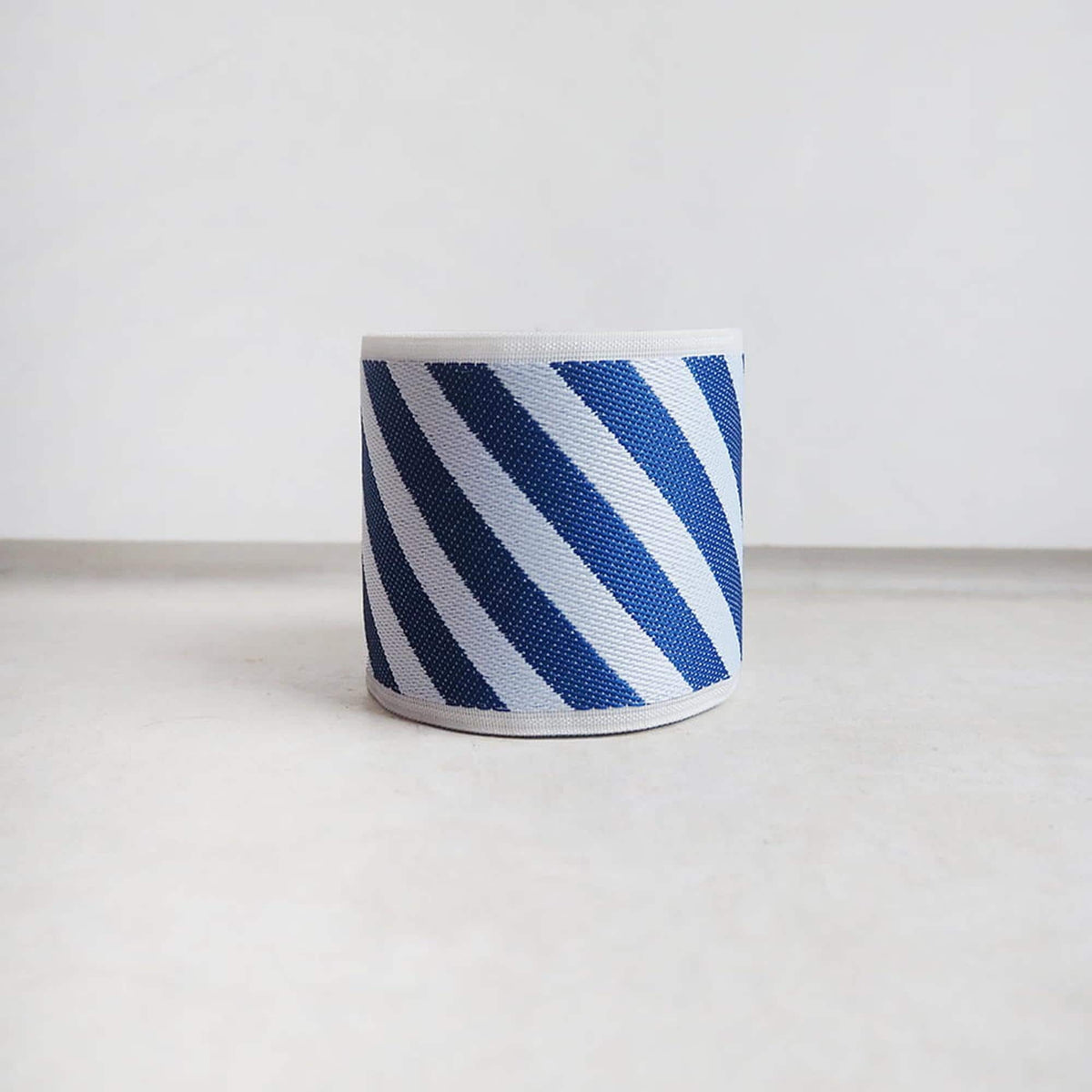 A blue and white striped lampshade is placed on a white surface against a plain white background.