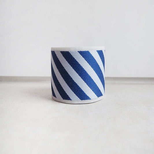 A blue and white striped lampshade is placed on a white surface against a plain white background.