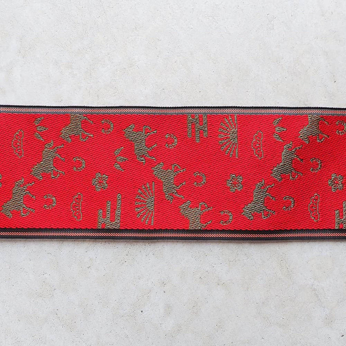 a red fabric with a repeating pattern of gold silhouettes of animals, such as horses and deer, against a white background.