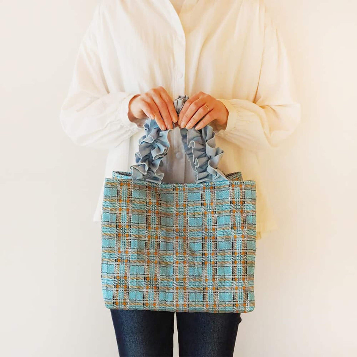 A person is holding a blue and orange checkered handbag in front of them.