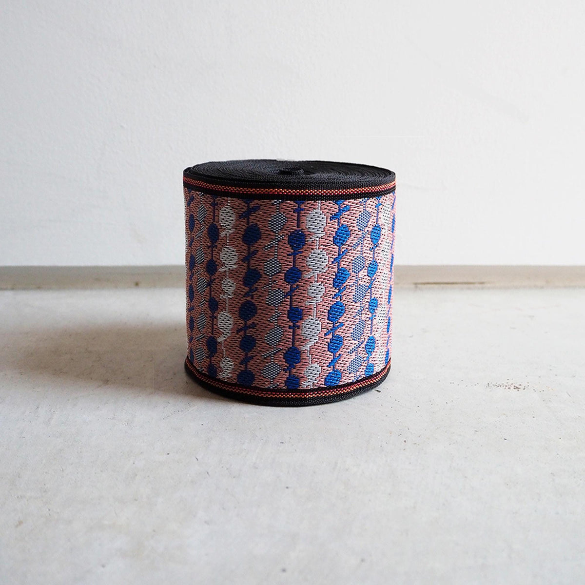 A colorful woven object with a pattern of blue, red, and white colors, sitting on a white surface against a plain background.