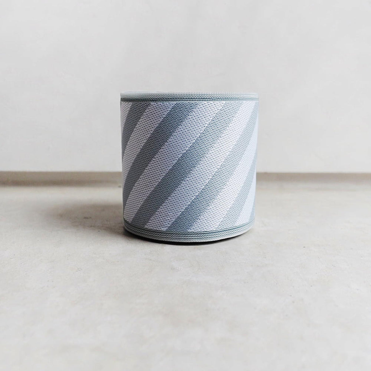 A cylindrical object with a striped pattern in shades of gray and white, placed on a plain surface.