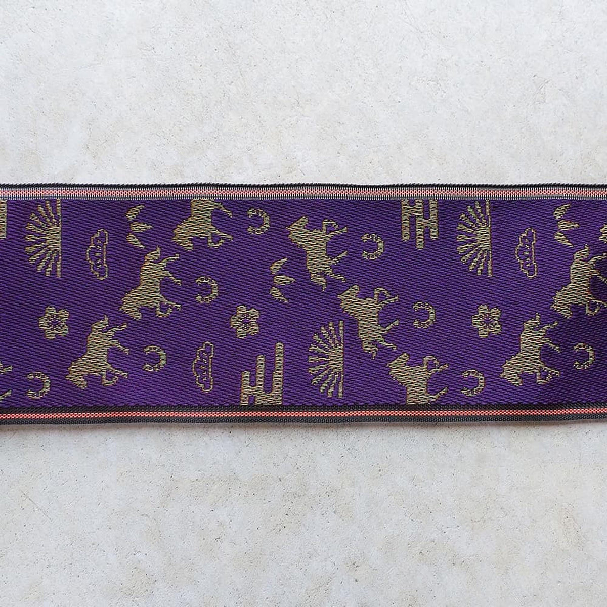 a purple fabric with a repeating pattern of gold silhouettes of horses and clouds.